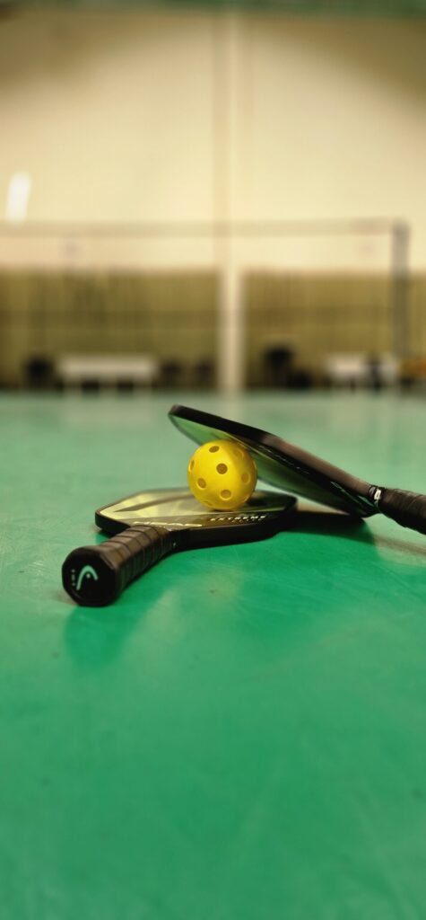 2 Pickleball Paddles mit einem Pickleball, die auf dem Boden liegen.