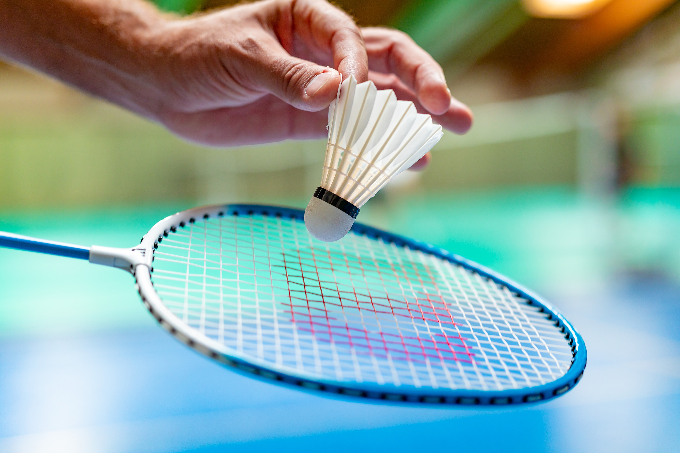 Badminton-Schläger mit einer Hand, die einen Shuffle mit Daumen und Zeigefinger hält.