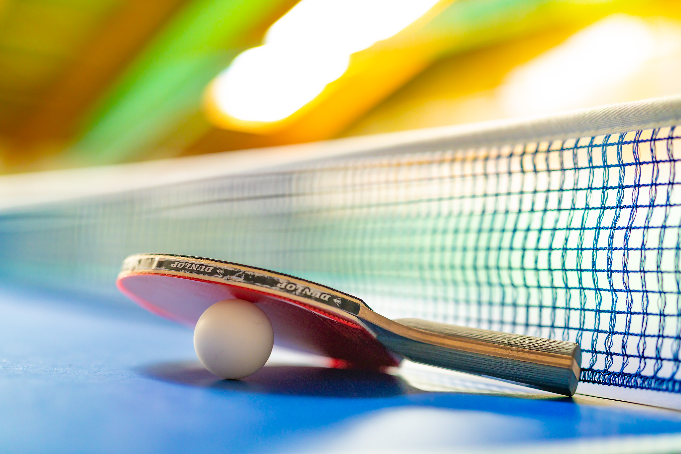 Tischtennisschläger, der auf dem Tischtennistisch liegt, mit einem Ball zwischen Schläger und Tischplatte