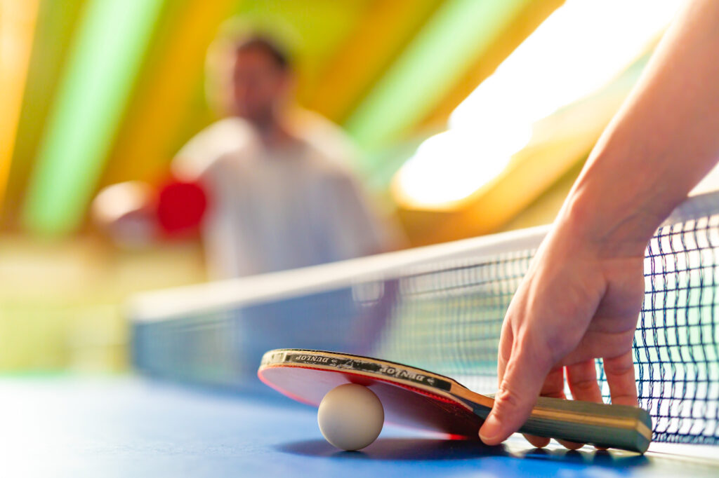 Hand hält Tischtennisschläger, der auf dem Tischtennistisch liegt, mit einem Ball zwischen Schläger und Tischplatte