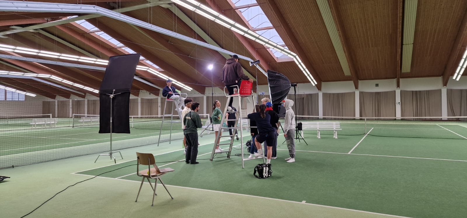 Filmteam aus 10 Leuten am Tennisplatz mit Lichtern, Schiedsrichterstohl